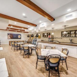 A modern restaurant interior with wooden beams, tables, and chairs, featuring a bar counter and stylish lighting fixtures.