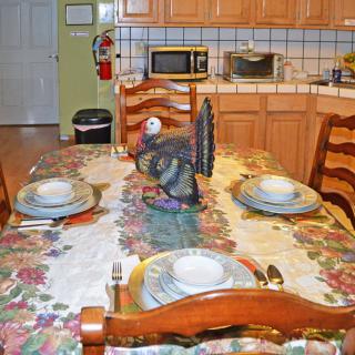 A kitchen with a dining table set for four, featuring a turkey decoration centerpiece and a floral tablecloth.
