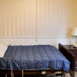 A cozy bedroom with a neatly made bed featuring a blue blanket, accompanied by a wooden nightstand and lamp.