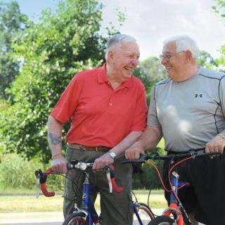 Two elderly men enjoying a moment with their bicycles outdoors.