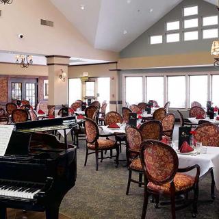 A spacious restaurant dining area featuring a grand piano and elegantly set tables.