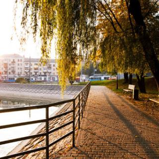 A serene walkway by the water, framed by trees and bathed in the warm glow of sunset.