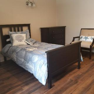 A simple bedroom with a bed, chair, and dresser on a wooden floor.