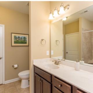 A clean and well-lit bathroom featuring a large mirror, sink with vanity, toilet, and shower.