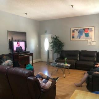 A group of people relaxing in a living room, watching television on a screen.