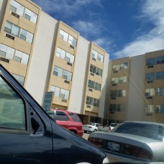 A view of apartment buildings with parked cars in the foreground and a clear blue sky.