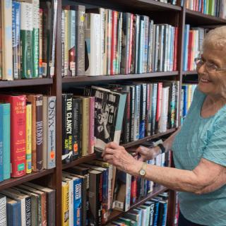 An elderly woman browsing books on a library shelf.