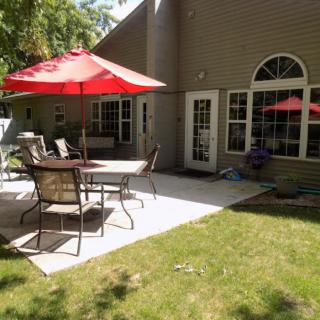 A sunny backyard patio with outdoor furniture and red umbrellas.