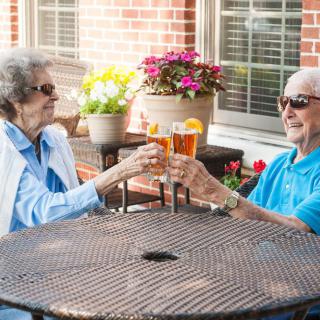 An elderly couple enjoying drinks and toasting on a patio.