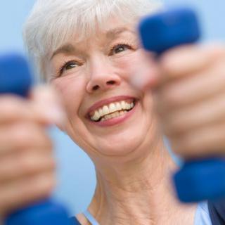 A senior woman smiling while exercising with dumbbells.