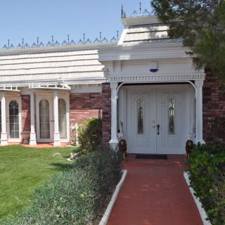 A charming building entrance with ornate architecture, featuring a garden and brick pathway leading to white double doors.