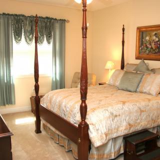 A traditionally decorated bedroom featuring a four poster bed, elegant curtains, and a warmly lit lamp.