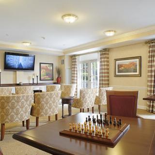 A cozy lounge with a chess board on the table, comfortable chairs, and a television in the background.