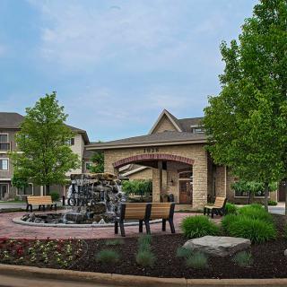 A serene outdoor area featuring a fountain, benches, and lush landscaping in front of a building.