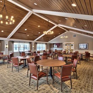 A spacious dining room with wooden ceilings, arranged with round tables and cushioned chairs.