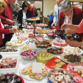 A group of people enjoying a buffet with a variety of desserts and sweets on display.