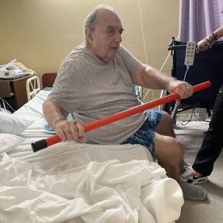 A patient in a hospital bed using a support pole for assistance.