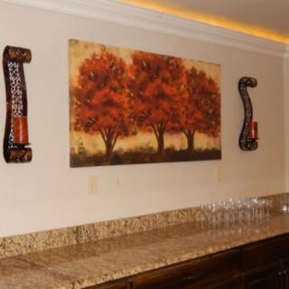 An interior wall featuring a painting of trees with decorative side pieces and a countertop lined with glasses.