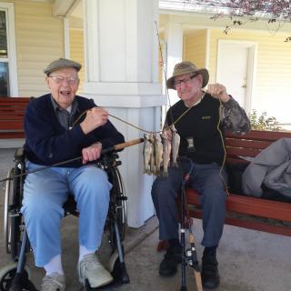 Two elderly friends enjoying a moment together with fishing rods outdoors.