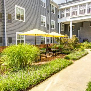 A well-maintained outdoor garden with patio furniture and umbrellas, surrounded by lush landscaping in front of a building.