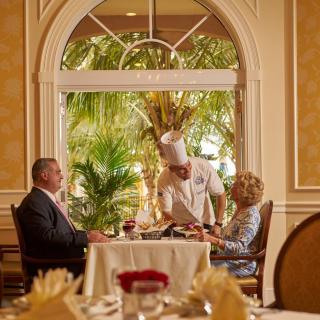 A couple is being served by a chef at an elegant restaurant with a lavish interior.