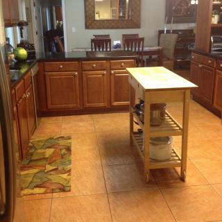 A cozy kitchen with wooden cabinets and a small island, featuring tile flooring and an adjoining dining area.