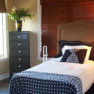 A cozy bedroom with a single bed, stylish bedding, and a dresser adorned with a vase of flowers.