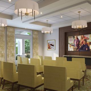 A modern meeting room with elegant seating and chandeliers, featuring a large screen at the front.