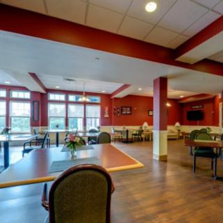 A cozy dining area with tables and chairs, featuring large windows and warm lighting.