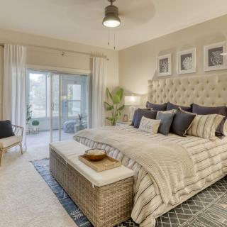 A cozy and elegantly designed bedroom featuring a large bed with plush pillows, neutral color palette, and abundant natural light streaming through the glass doors.
