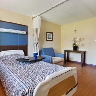 A clean and well-organized hospital room with a bed, seating area, and minimalist decor.