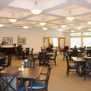An empty dining room with neatly arranged tables and chairs, featuring elegant lighting and decor.