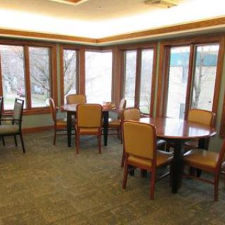 A dining area with several tables and chairs surrounded by large windows allowing natural light in.