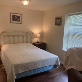 A cozy bedroom with a bed, bedside table, and lamp next to a window.