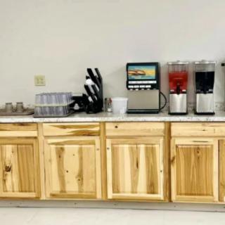 A kitchen counter with a beverage station including drink dispensers and cups, alongside wooden cabinets.