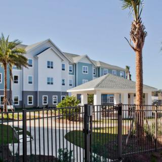 A view of a residential apartment complex with palm trees and a fence in the foreground.