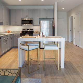 A modern kitchen featuring sleek gray cabinetry, stainless steel appliances, and a small dining area with stylish seating.