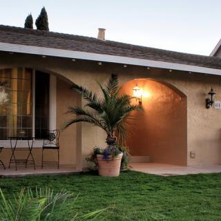 A charming house with a well-lit patio and potted plants in the front yard during the evening.