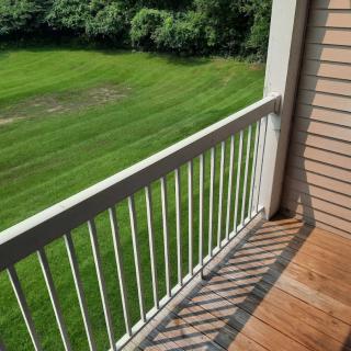 A balcony with white railings overlooking a grassy area on a sunny day.