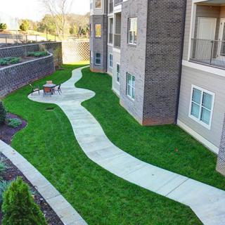 A beautifully landscaped outdoor area with a winding pathway next to an apartment building.