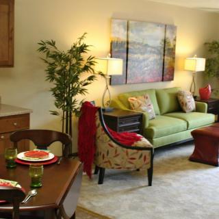 A cozy and well-decorated living room with a green sofa, dining area, and elegant artwork on the wall.