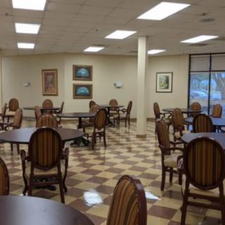 An empty cafeteria with neatly arranged tables and chairs, illuminated by overhead lights, featuring artwork on the walls.
