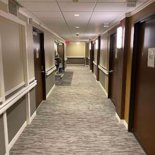 A well-lit hotel hallway featuring multiple doors and a patterned carpet.
