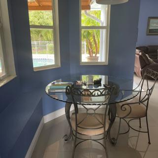 A cozy dining nook with a glass table and chairs, surrounded by blue walls and illuminated by natural light from multiple windows.