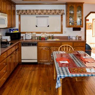 A cozy kitchen with wooden cabinets and a dining table, featuring various appliances.