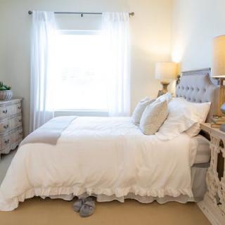 A cozy and well-decorated bedroom with a neatly made bed, two lamps, and a window letting in natural light.