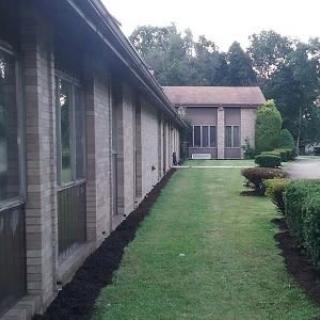 A view of a brick building with a neatly maintained lawn and trimmed bushes, surrounded by trees.