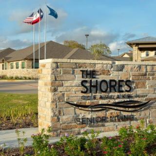 Entrance sign for The Shores community with flags waving in the background.