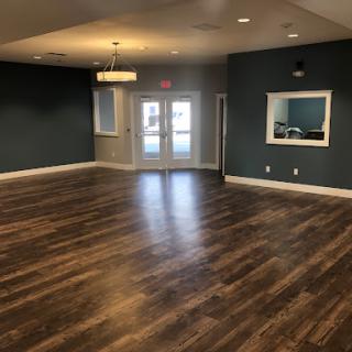 A spacious, modern interior room featuring wooden flooring and dark green walls, designed for versatility.