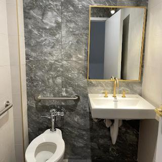 A modern bathroom featuring a toilet, sink, and mirror with stylish gray walls and gold fixtures.
